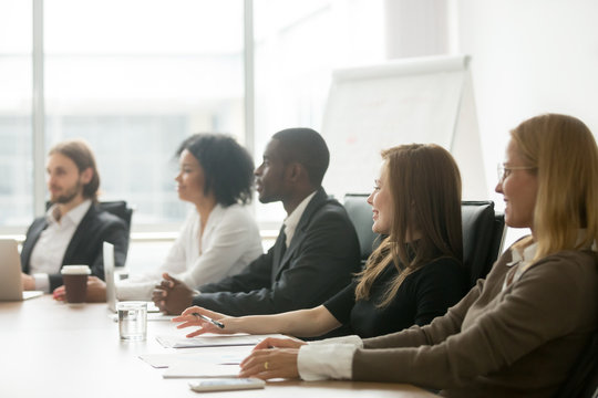 Diverse smiling business people sitting at conference table at group meeting or corporate briefing, african and caucasian businessmen and businesswomen partners team attending training concept