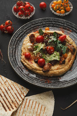 Hummus with vegetables and seafood on black background