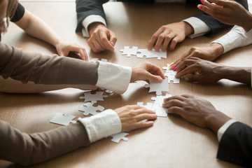 Diverse business people helping in assembling puzzle, cooperation in decision making, team support...