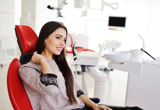 Portrait of a beautiful girl in a red dental chair on the background of a modern clinic