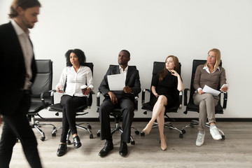Rivalry at job interview concept, applicant walking in room while envious curious multiracial people sitting in row looking at rival waiting for result, winner and loser, jealous of other success