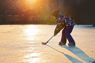 Naklejka premium Children, playing hockey and skating in the park on frozen lake, wintertime on sunset