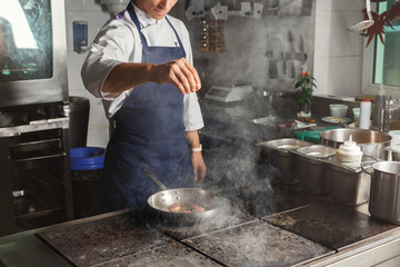 Chef cooking meat at restaurant or hotel kitchen