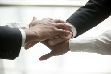 African and caucasian partners join hands in pile together, motivated multiracial business team promising help and support, engagement or unity in collaboration, commitment in teamwork, close up view