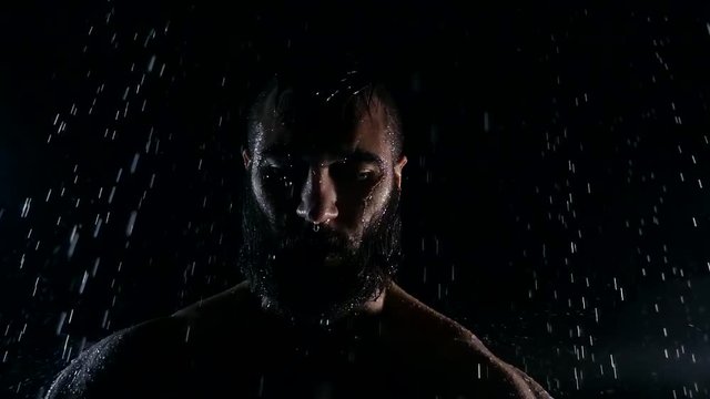 formidable and terrifying man on a darkness street in night, his silhouette under water drops