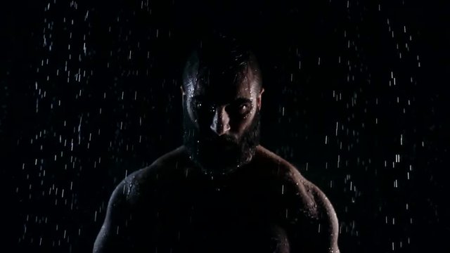 Figure of muscular adult man with strong embossed hands in a darkness under water flows, he is looking forward