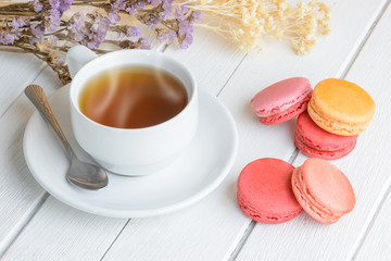 Different types color of macaroons with Cup of hot tea on white wooden background