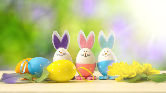 Cute Easter bunny ornaments and Easter Eggs on white table against garden background with lens flare.