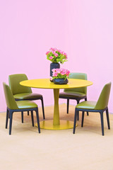 laconic interior of the dining room. Yellow round table and green leather chairs, vase with flowers on the table. Isolate on pink background