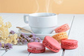 Different types color of macaroons with Cup of hot tea on white wooden background