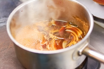 Lamb shank boiling in broth. Close up of shank of lamb boiling in casserole at professional kitchen. European restaurant cuisine.