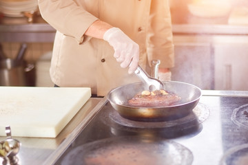 Chef frying meat with garlic. Hands of male chef frying duck breast at professional kitchen. Man at restaurant cooking delicious meat.