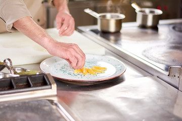 Male hands putting orange segments on plate. Chef at restaurant serving plate with orange pieces. Cook decorating plate with fresh orange.