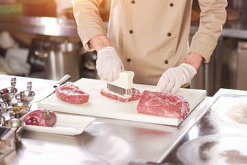 Chef making steak from raw meat. Male chef pressing beef meat on white board at kitchen. Chef...