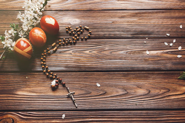 stylish easter eggs  and wooden rosary with cross and  cherry flowers on wooden background flat lay. modern eggs natural dyed. space for text. happy easter greeting. christ is risen