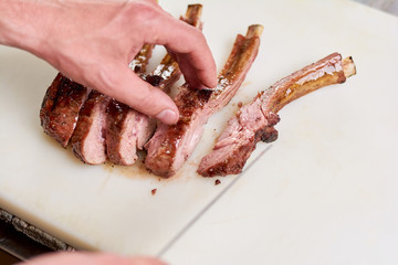 Sliced pieces of juicy grilled ribs. Roasted barbecue calf ribs and male hands on white background close up. Chef cooked meat at kitchen.