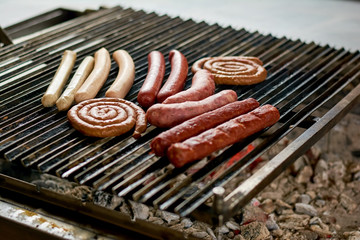 Assorted sausages grilling over coals on barbecue. Assortment of different sausages grilling on iron grill.