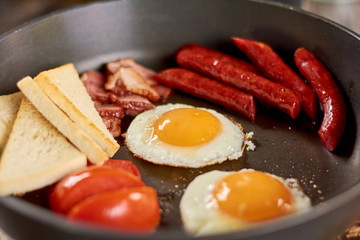 English breakfast in frying pan. English breakfast - fried eggs, baked sausages and bacon, tomatoes and toasts.