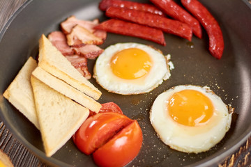 Traditional english breakfast. English breakfast including fried eggs, baked sausages and bacon, toasts and tomatoes.