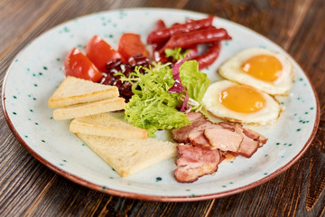 English breakfast served with green salad. English breakfast with fried eggs, baked sausages and bacon, tomatoes, beans and toasts. Traditional british breakfast.