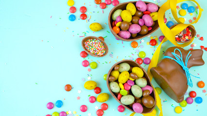 Happy Easter overhead with chocolate Easter eggs and decorations on a wood table background with copy space.