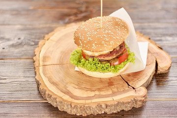 Big tasty burger on round wood. Big hamburger with beef cutlet and fresh vegetables on natural wood. Classic american burger.