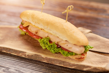Classic hot dog on wooden board. Tasty hot dog with chicken sausage and fresh lettuce, tomatoes, cucumbers and cheese. Fast food menu.