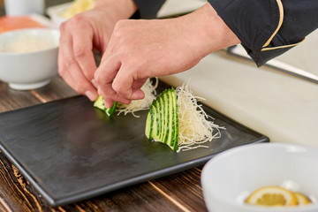 Chef decorating plate with sliced cucumber. Cook making decoration from sliced cucumber on plate for sushi.
