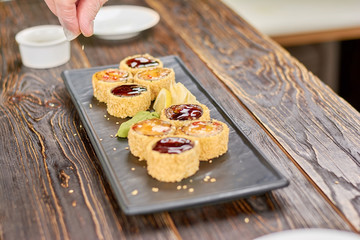 Chef adding sesame to sushi rolls. Delicilous set of unagi sushi rolls on plate. Restaurant of japanese food.