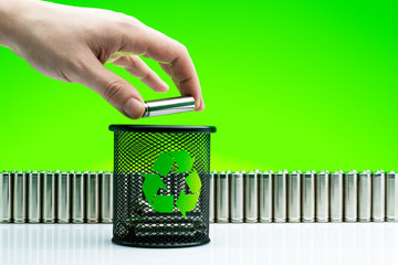 Ecology recycling concept, nature energy, man hand drop used or new battery on recycle garbage bin, rechargeable AA accumulator, alkaline batteries in row on green background