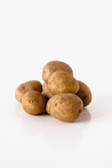 Small pile of uncooked, unpeeled and dirty medium-sized Yukon Gold potatoes or taters on white background