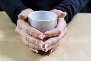 Fototapeta na wymiar Empty white mug in women's hands. Hands holding a china mug on a wooden kitchen table.