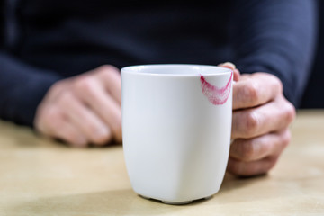 Empty white mug with gloves. Hands in warm gloves holding a china mug on a wooden kitchen table.