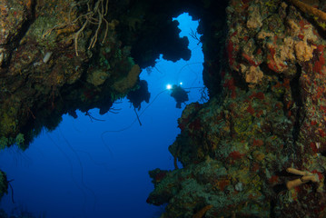 A bold underwater explorer is on a scuba diving adventure and finds an opening in the tropical reef. Using high powered lights, the diver will investigate the passage to see where is leads