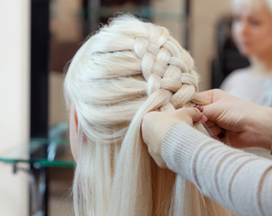 Beautiful girl with blonde hair, hairdresser weaves a  braid close-up, in a beauty salon. Professional hair care and creating hairstyles.