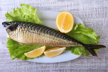 Smoked mackerele and lemon on green lettuce leaves on Wooden cutting board isolated on white background.
