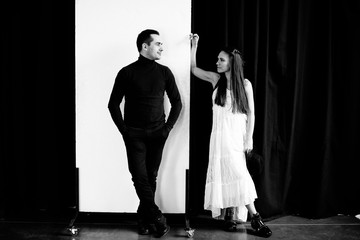 Love story. Creative photo on which the guy in black clothes is standing on a white background, and the girl in the white dress is standing on a black background. They look at each other