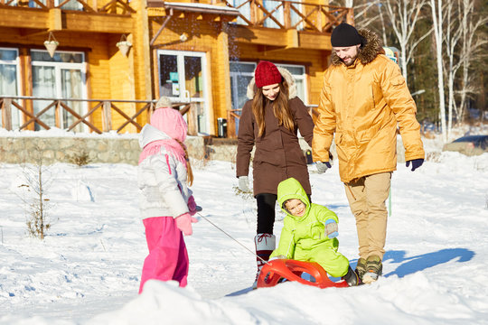 Young Caucasian Couple Walking With Little Children On Beautiful Winter Day Out Of Town, Girl Dragging Sled With Her Brother