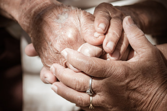 Hands of Asian woman holding elderly grandfather man hands wrinkled skin with feeling take care of Love. World Kindness Day and Adult care center, Senior citizen is common euphemism for an old person.