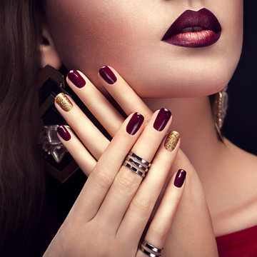 Beautiful woman with perfect make-up and burgundy and golden manicure wearing jewellery