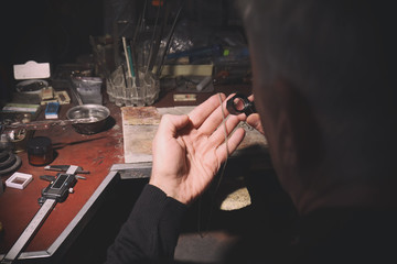 Jeweler examining golden chain with magnifier in workshop