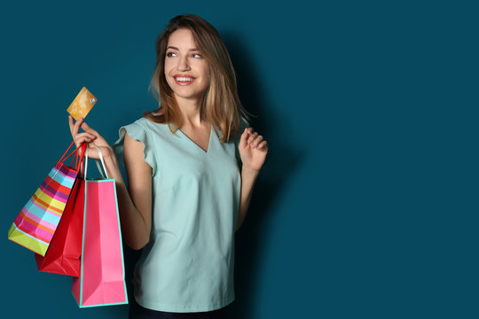 Happy young woman with credit card and shopping bags on color background