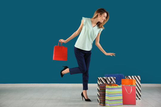 Happy young woman with shopping bags against color wall