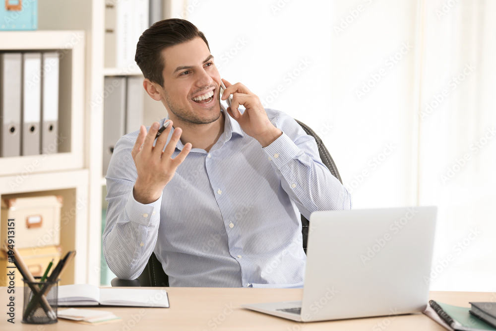 Poster Young man talking on mobile phone while working in office