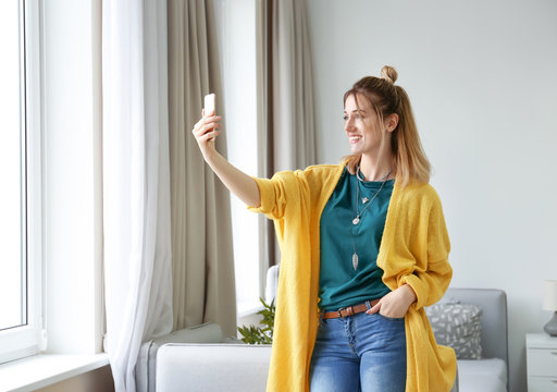 Young woman in yellow cardigan taking selfie indoors