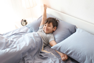 Cute little boy stretching in bed at home