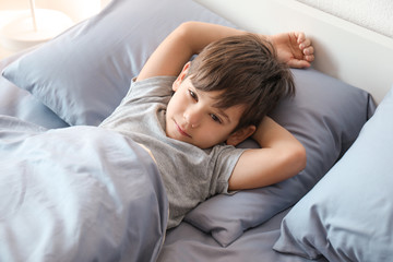 Cute little boy lying in bed at home