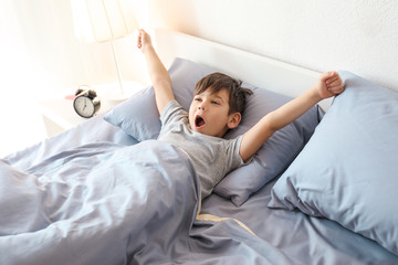 Cute little boy stretching in bed at home