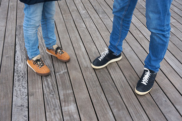 Child's and man's feet. Jeans and shoes on wooden floor