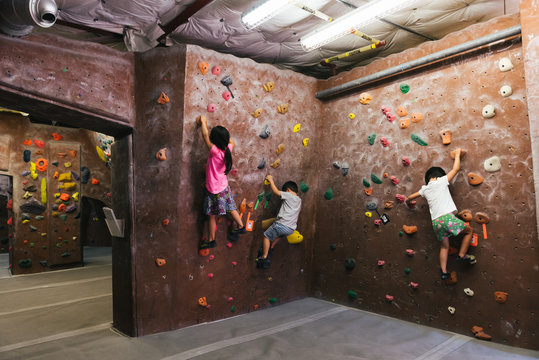 Elementary aged Asian children bouldering on rock climbing wall indoors
